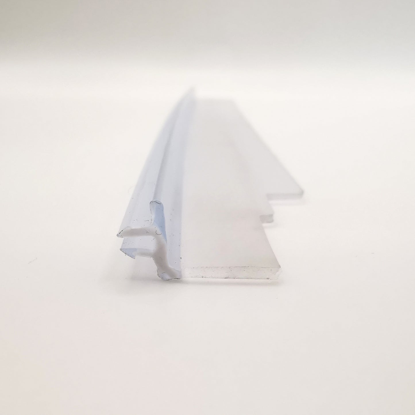 Dichtleiste der Marke HÜPPE, transparentes, schmales, längliches, L-förmiges Kunststoffprofil, mit zwei Lamellen an der linken Profilaußenseite, vor weißem Hintergrund, Frontansicht.