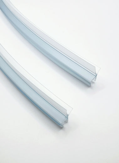 Ablaufprofil-Set der Marke HÜPPE bestehend zwei gebogenen, transparenten, schmalen, länglichen, U-förmigen Kunststoffprofil, mit einem Ablaufschutz an der Profilunterseite, vor weißem Hintergrund, Vogelperspektive.