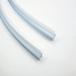 Ablaufprofil-Set der Marke HÜPPE bestehend zwei gebogenen, transparenten, schmalen, länglichen, U-förmigen Kunststoffprofil, mit einem Ablaufschutz an der Profilunterseite, vor weißem Hintergrund, Vogelperspektive.