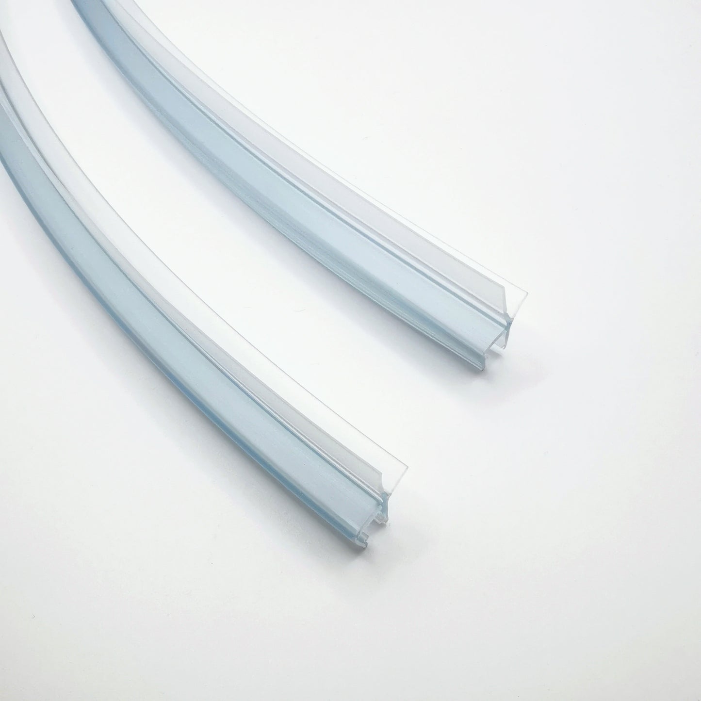 Ablaufprofil-Set der Marke HÜPPE bestehend zwei gebogenen, transparenten, schmalen, länglichen, U-förmigen Kunststoffprofil, mit einem Ablaufschutz an der Profilunterseite, vor weißem Hintergrund, Vogelperspektive.