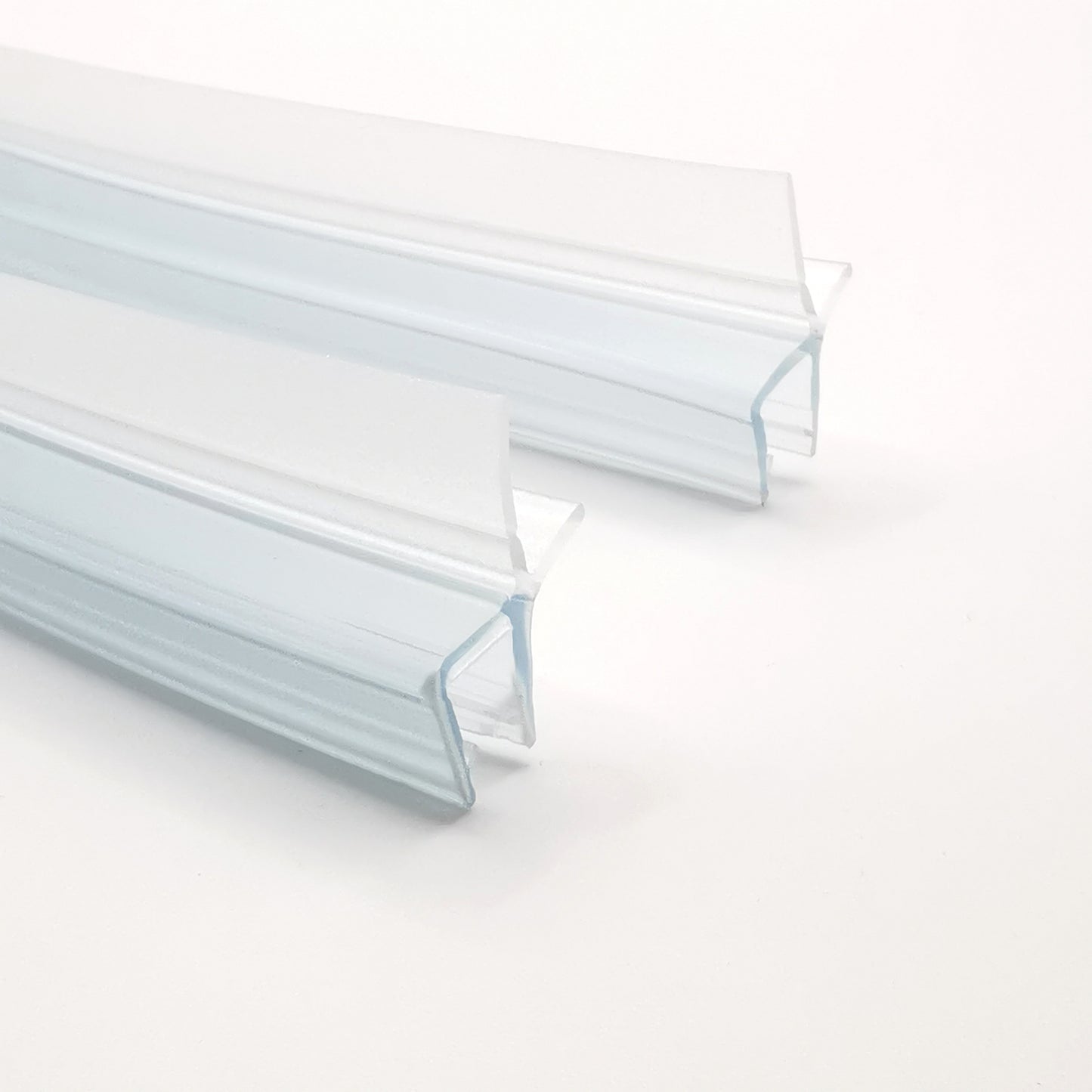 Detailaufnahme Ablaufprofil-Set der Marke HÜPPE bestehend zwei gebogenen, transparenten, schmalen, länglichen, U-förmigen Kunststoffprofil, mit einem Ablaufschutz an der Profilunterseite, vor weißem Hintergrund.