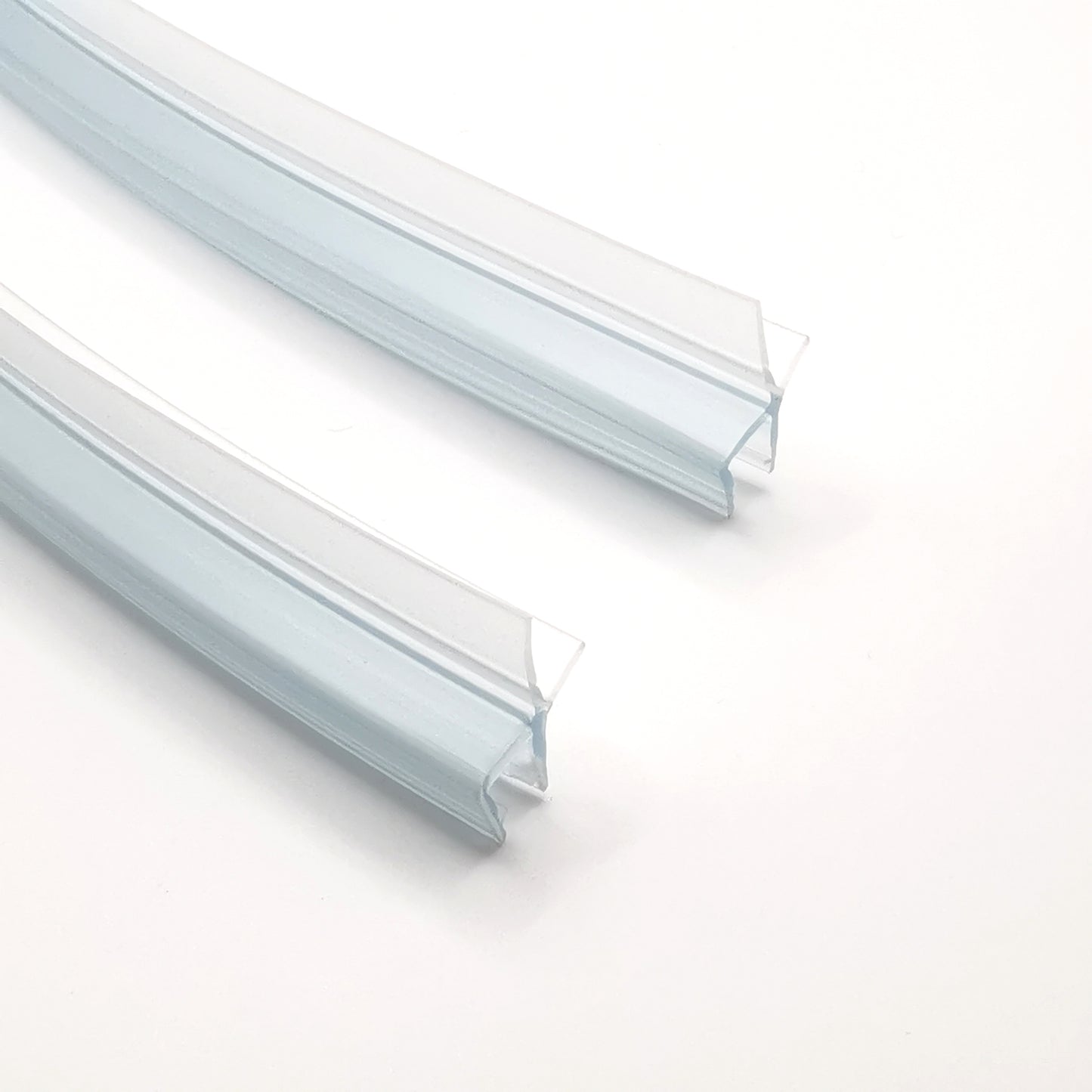 Nahaufnahme Ablaufprofil-Set der Marke HÜPPE bestehend zwei gebogenen, transparenten, schmalen, länglichen, U-förmigen Kunststoffprofil, mit einem Ablaufschutz an der Profilunterseite, vor weißem Hintergrund.