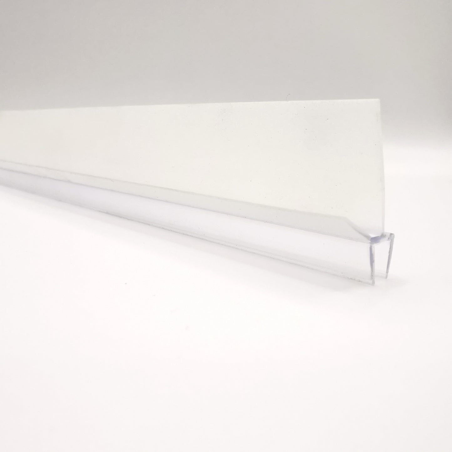 Nahaufnahme einer Ablaufleiste der Marke HÜPPE, transparentes, schmales, längliches, U-förmiges Kunststoffprofil, mit einem Ablaufschutz an den Profilaußenkanten, vor weißem Hintergrund.