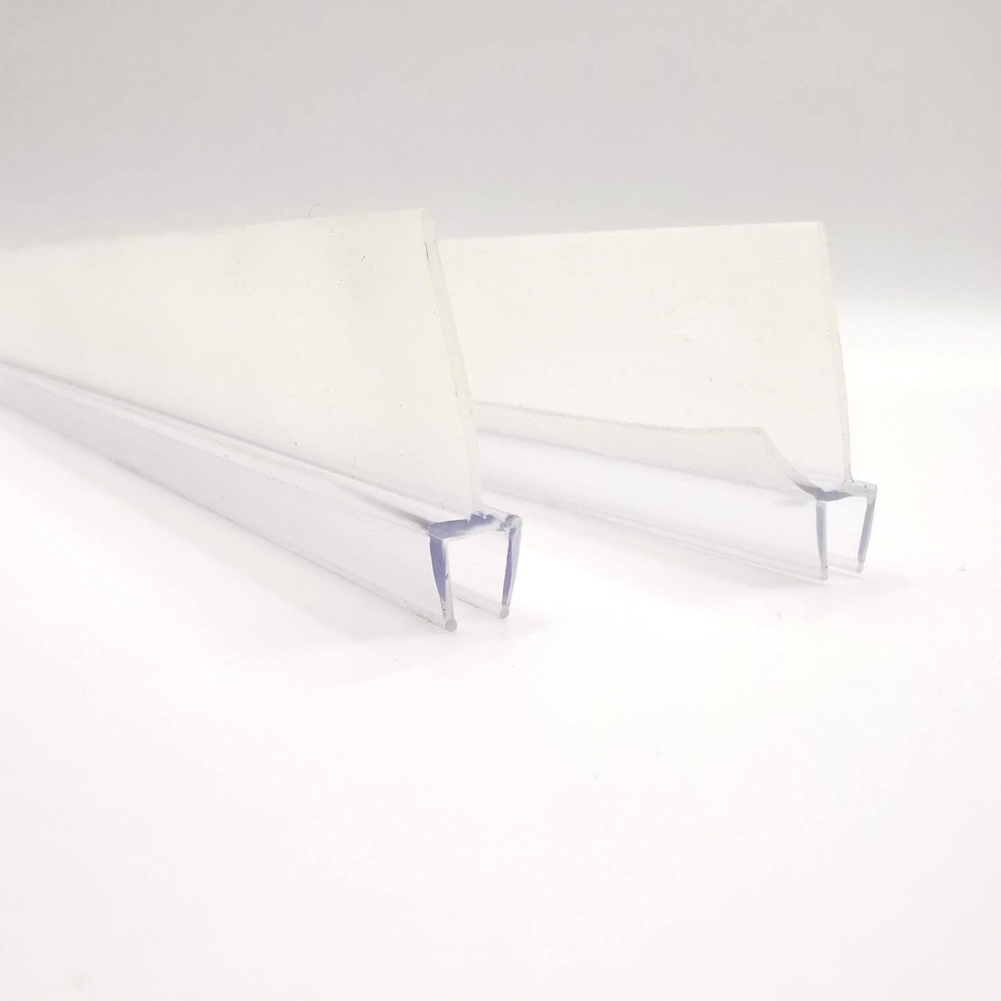 Detailaufnahme zweier Ablaufleisten der Marke HÜPPE, transparente, schmale, längliche, U-förmige Kunststoffprofile, mit einem Ablaufschutz an den Profilaußenkanten, vor weißem Hintergrund.