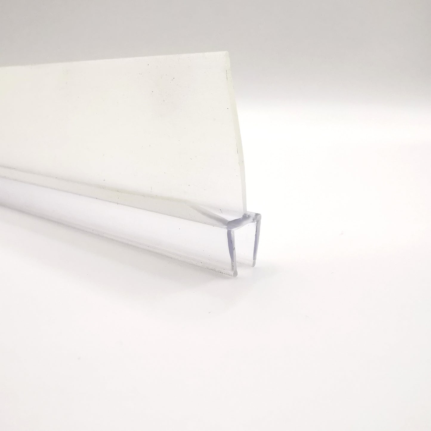 Detailaufnahme einer Ablaufleiste der Marke HÜPPE, transparentes, schmales, längliches, U-förmiges Kunststoffprofil, mit einem Ablaufschutz an den Profilaußenkanten, vor weißem Hintergrund.