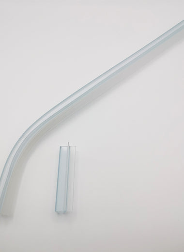 Nahaufnahme von zwei Ablaufprofilen der Marke HÜPPE, transparente, schmale, längliche, U-förmige Kunststoffprofile, mit einem Ablaufschutz an der Profilaußenkante, in zwei Längen sowie a-symmetrisch gebogen, vor weißem Hintergrund