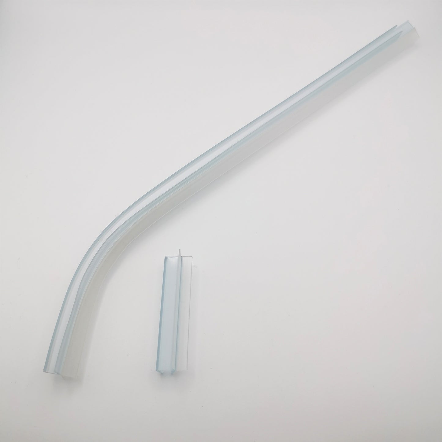 Nahaufnahme von zwei Ablaufprofilen der Marke HÜPPE, transparente, schmale, längliche, U-förmige Kunststoffprofile, mit einem Ablaufschutz an der Profilaußenkante, in zwei Längen sowie a-symmetrisch gebogen, vor weißem Hintergrund