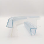 Detailaufnahme von zwei Ablaufprofilen der Marke HÜPPE, transparente, schmale, längliche, U-förmige Kunststoffprofile, mit einem Ablaufschutz an der Profilaußenkante, in zwei Längen sowie a-symmetrisch gebogen, vor weißem Hintergrund, Frontansicht.