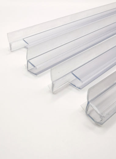 Detailaufnahme Ablaufprofil-Set der Marke HÜPPE, bestehend aus vier transparenten, schmalen, länglichen, U-förmigen Kunststoffprofilen, mit einem Ablaufschutz an den Außenkanten der Profilunterseite, vor weißem Hintergrund