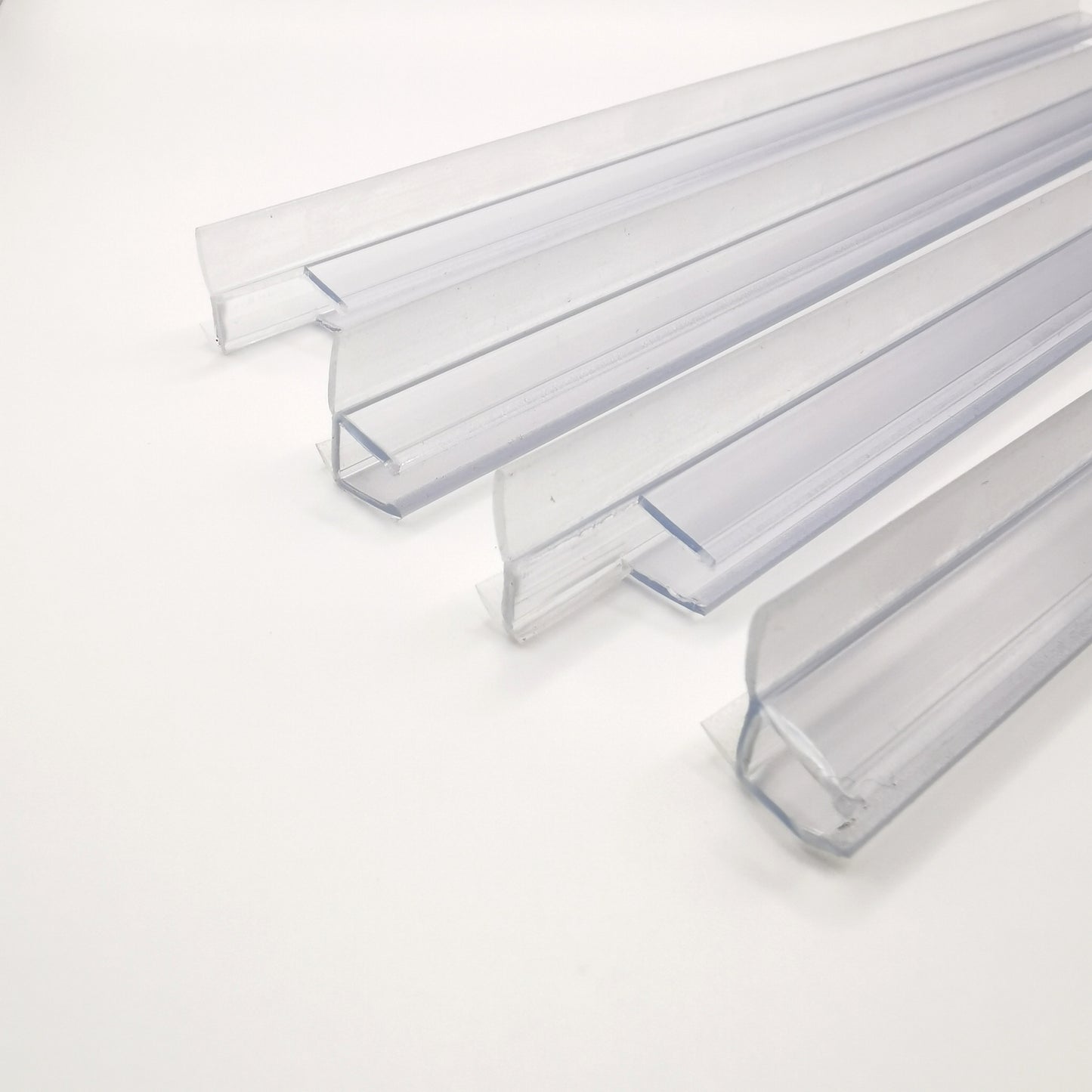 Detailaufnahme Ablaufprofil-Set der Marke HÜPPE, bestehend aus vier transparenten, schmalen, länglichen, U-förmigen Kunststoffprofilen, mit einem Ablaufschutz an den Außenkanten der Profilunterseite, vor weißem Hintergrund