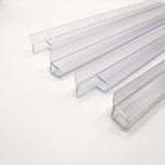 Detailaufnahme Ablaufprofil-Set der Marke HÜPPE, bestehend aus vier transparenten, schmalen, länglichen, U-förmigen Kunststoffprofilen, mit einem Ablaufschutz an den Außenkanten der Profilunterseite, vor weißem Hintergrund