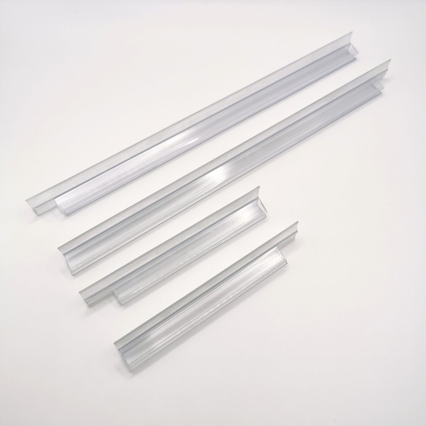 Nahaufnahme Ablaufprofil-Set der Marke HÜPPE, bestehend aus vier transparenten, schmalen, länglichen, U-förmigen Kunststoffprofilen, in zwei Längen, mit einem Ablaufschutz an den Außenkanten der Profilunterseite, vor weißem Hintergrund