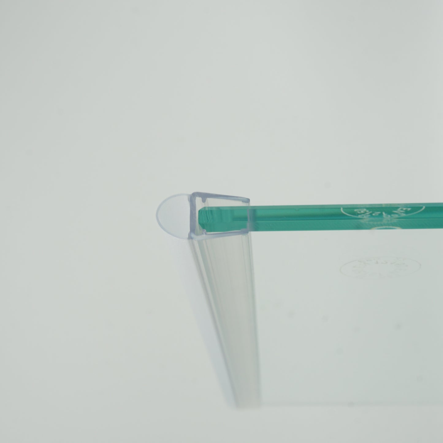 Nahaufnahme eines O-Profils der Marke HÜPPE, montiert an Glasdusche, transparentes, schmales, längliches, U-förmiges Kunststoffprofil, mit einem O-förmigen Profil an der Profilvorderseite, vor weißem Hintergrund.