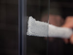 Graues, schmales und längliches Reinigungsgerät mit Mikrofaserbezug wird zwischen zwei überlappenden Glasflächen, der HÜPPE Duschabtrennung Xtensa Pure, geführt, um den Zwischenraum zu reinigen.