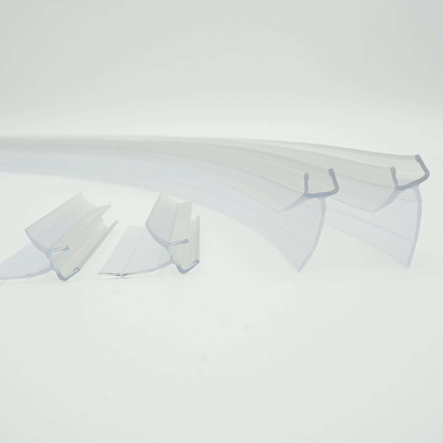 Ablaufprofil-Set der Marke HÜPPE bestehend aus vier gebogenen, transparenten, schmalen, länglichen, U-förmigen Kunststoffprofil, mit einem Ablaufschutz an der Profilunterseite, in zwei Längen, vor weißem Hintergrund.