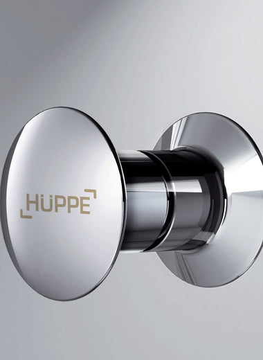 Nahaufnahme einer Duschkabine mit einem Silber hochglänzenden runden HÜPPE Knaufgriff im Fokus, vor einem hellen Hintergrund.