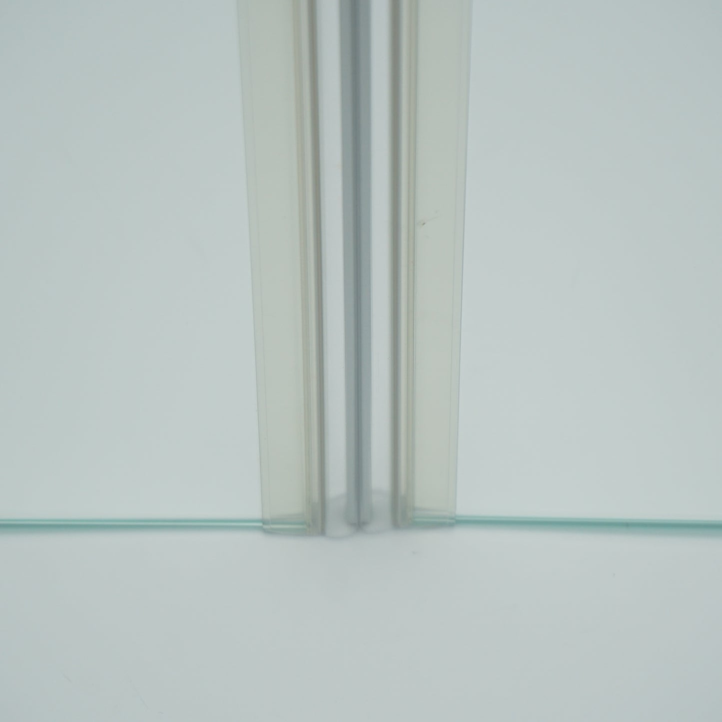 Nahaufnahme von zwei Magnetleisten der Marke HÜPPE, montiert an Glasdusche, transparente, schmale, längliche, U-förmige Kunststoffprofile, mit Magnetprofilen an der Vorderseite, Magneten bilden zusammen geschlossenen 180 Grad Winkel, vor weißem Hintergrund, Frontansicht.