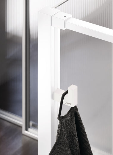 Select+ Hook, Weißer, matter Haken der Marke HÜPPE, der an einem senkrechten Profil einer Glasdusche montiert ist, daran hängt ein graues Handtuch, in einem modernen Badezimmer mit dunkelbraunem Fußboden.
