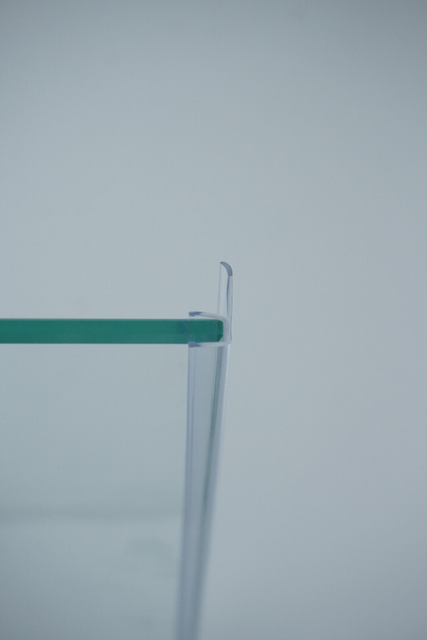 Nahaufnahme einer Dichtleiste der Marke HÜPPE, transparentes, schmales, längliches, U-förmiges, Kunststoffprofil, mit einem Ablaufschutz an der Profilvorderseite, montiert an Glasdusche, vor hellem Hintergrund, Seitenansicht links.