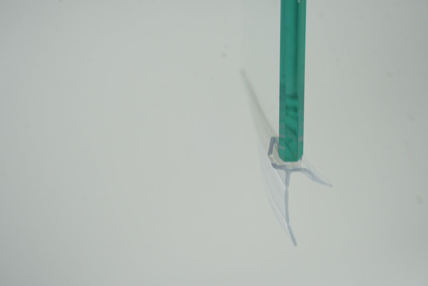 Nahaufnahme einer Ablaufleiste der Marke HÜPPE, transparentes, schmales, längliches, U-förmiges Kunststoffprofil, mit einem Ablaufschutz an der Profilunterseite, montiert an der Unterseite einer Glasdusche, vor weißem Hintergrund, Seitenansicht.