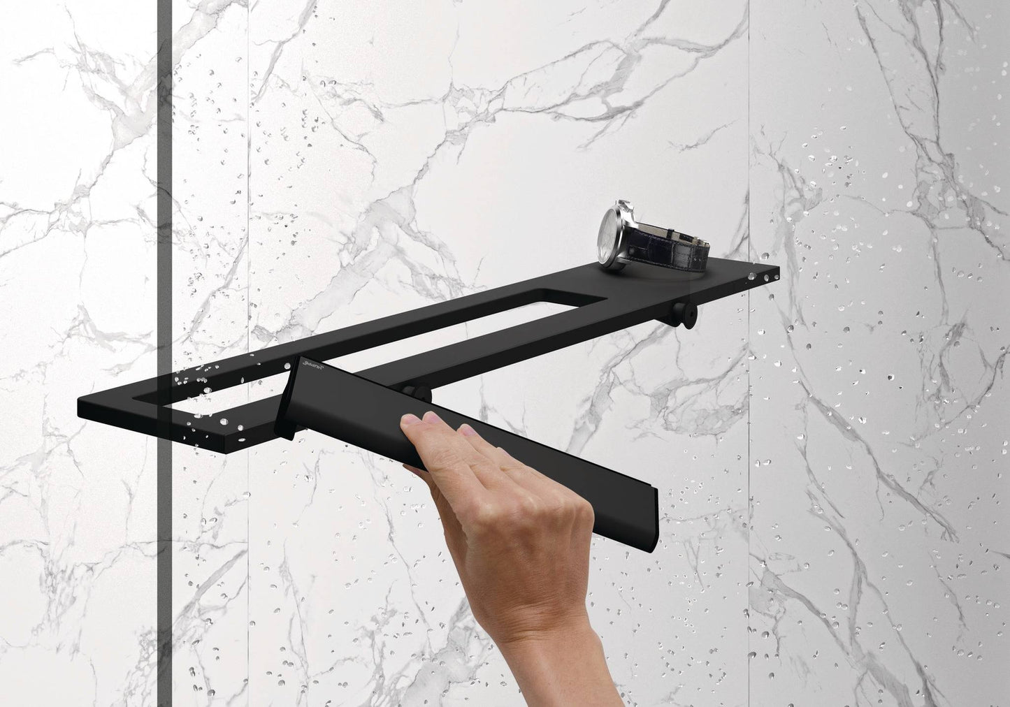 Hand wischt Wassertropfen von einer Glasdusche mit dem Select+ Wiper in schwarz matt, der Marke HÜPPE, während eine Uhr auf einer modernen Ablage vor einer hellen, strukturierten Wand liegt.