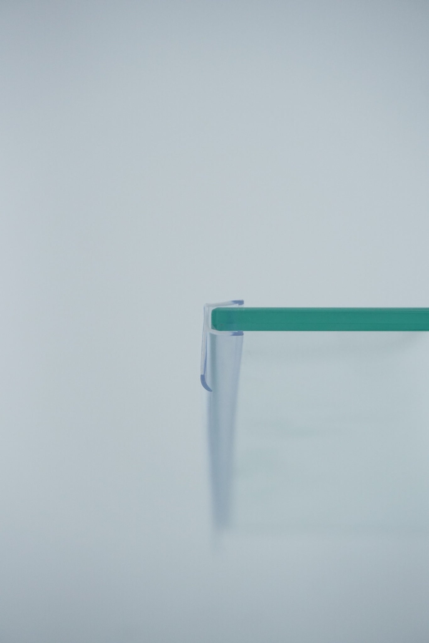 Nahaufnahme einer Dichtleiste der Marke HÜPPE, transparentes, schmales, längliches, U-förmiges, Kunststoffprofil, mit einem Ablaufschutz an der Profilvorderseite, montiert an Glasdusche, vor hellem Hintergrund, Seitenansicht rechts.