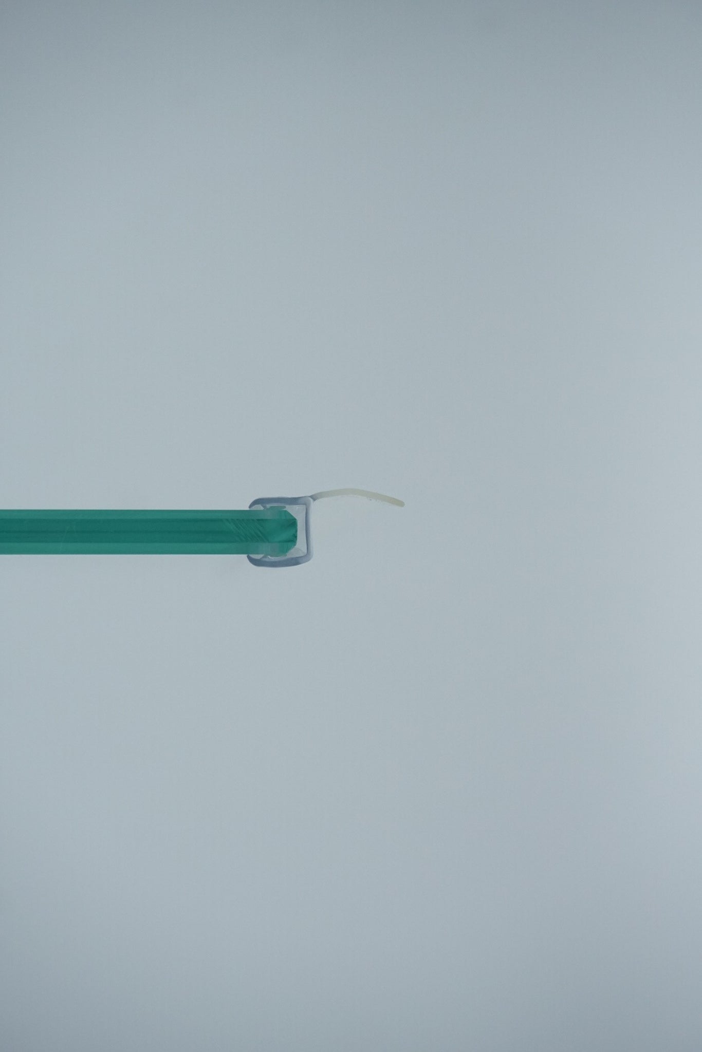 Nahaufnahme einer Dichtleiste der Marke HÜPPE, transparentes, schmales, längliches, U-förmiges Kunststoffprofil, mit einem Ablaufschutz an der Profilvorderseite, montiert an Glasdusche, vor weißem Hintergrund, Querschnitt.