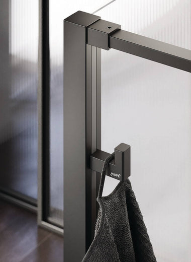 Select+ Hook, Schwarzer, matter Haken der Marke HÜPPE, der an einem senkrechten Profil einer Glasdusche montiert ist, daran hängt ein graues Handtuch, in einem modernen Badezimmer mit dunkelbraunem Fußboden.