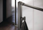 Select+ Hook, Schwarzer, matter Haken der Marke HÜPPE, der an einem senkrechten Profil einer Glasdusche montiert ist, daran hängt ein graues Handtuch, in einem modernen Badezimmer mit dunkelbraunem Fußboden.
