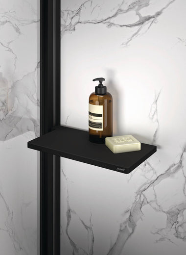 Select+ Tablet, Schwarze, matte Ablage der Marke HÜPPE befestigt an einer Wandleiste einer Glasdusche, darauf steht ein Seifenspender und eine Handseife, vor einer hellen strukturierten Wand.