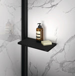 Select+ Tablet, Schwarze, matte Ablage der Marke HÜPPE befestigt an einer Wandleiste einer Glasdusche, darauf steht ein Seifenspender und eine Handseife, vor einer hellen strukturierten Wand.