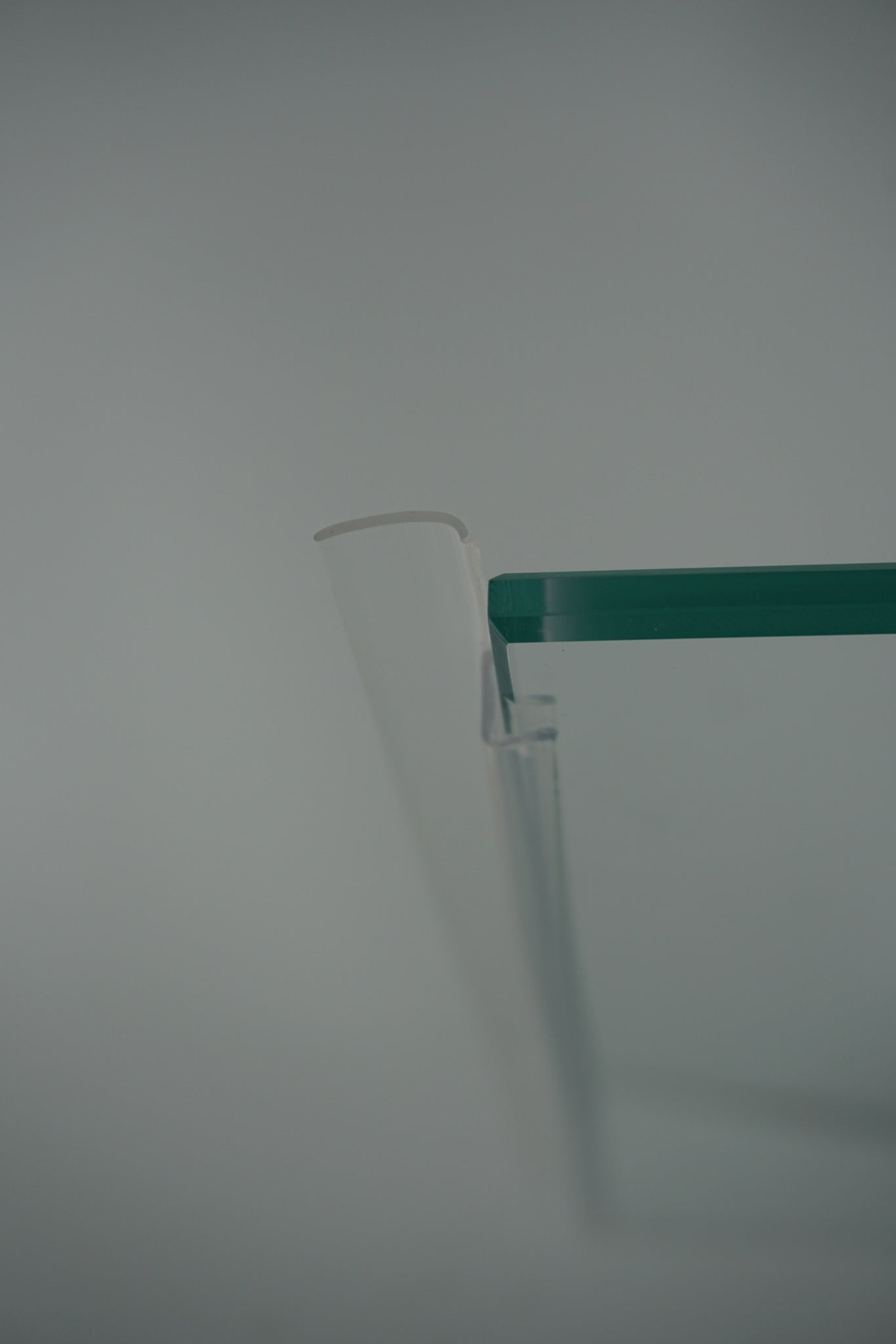 Nahaufnahme einer Anlagenleiste der Marke HÜPPE, transparentes, schmales, längliches, U-förmiges Kunststoffprofil, mit einem Ablaufschutz an der Profilvorderseite, vor weißem Hintergrund.