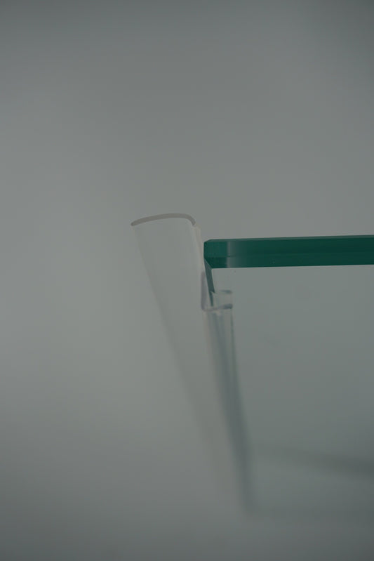 Nahaufnahme einer Anlagenleiste der Marke HÜPPE, transparentes, schmales, längliches, U-förmiges Kunststoffprofil, mit einem Ablaufschutz an der Profilvorderseite, vor weißem Hintergrund.