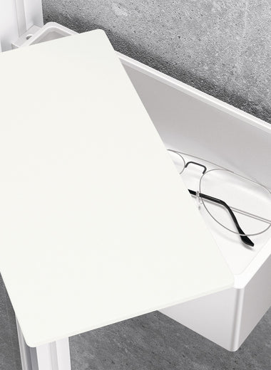 Weiße, matte Select+ Drybox der Marke HÜPPE befestigt an einer Wandleiste einer Glasdusche, mit weißem, offenstehendem Deckel, darin liegt eine Brille, vor einer hellgrauen, strukturierten Wand.