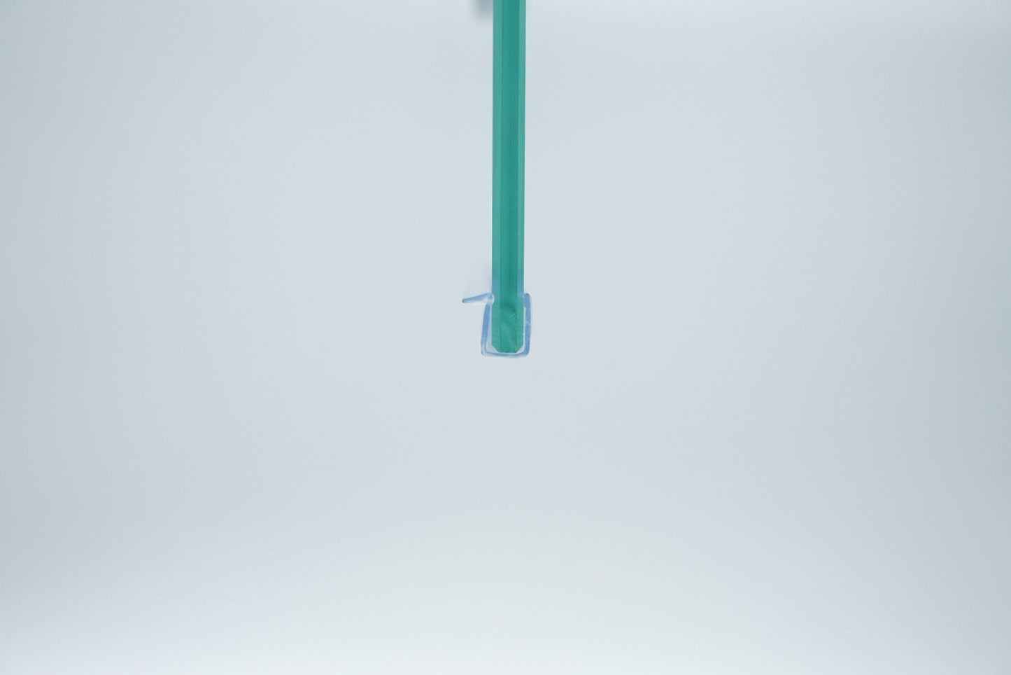 Nahaufnahme einer Ablaufleiste der Marke HÜPPE, transparentes, schmales, längliches, U-förmiges Kunststoffprofil, mit einem Vorsprung an der rechten Profiloberkante, montiert an der Unterseite einer Duschkabine, vor weißem Hintergrund, Frontansicht.