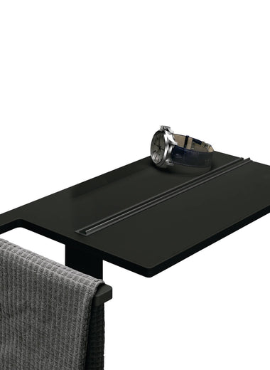 Select+ Showerboard, Klemmbares Ablagebrett der Marke HÜPPE in schwarz matt, auf der eine Uhr und ein graues Handtuch abgelegt sind.