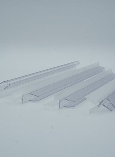 Nahaufnahme von vier Ablaufprofilen der Marke HÜPPE, transparente, schmale, längliche, U-förmige Kunststoffprofile, mit einem Ablaufschutz an der Profilaußenkante, vor weißem Hintergrund