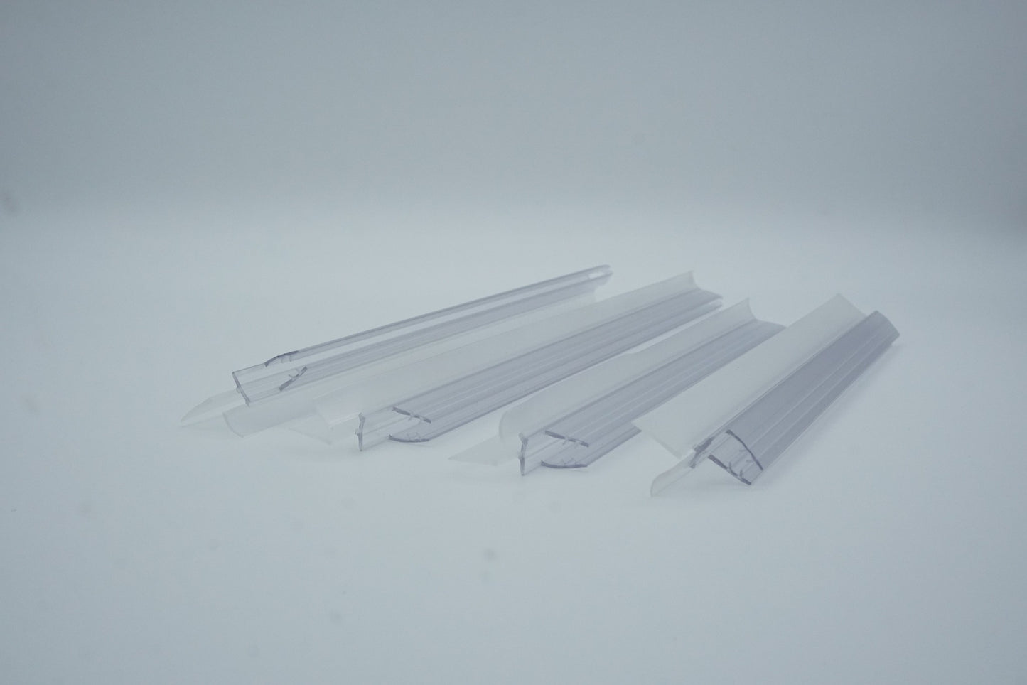 Nahaufnahme von vier Ablaufprofilen der Marke HÜPPE, transparente, schmale, längliche, U-förmige Kunststoffprofile, mit einem Ablaufschutz an der Profilaußenkante, vor weißem Hintergrund