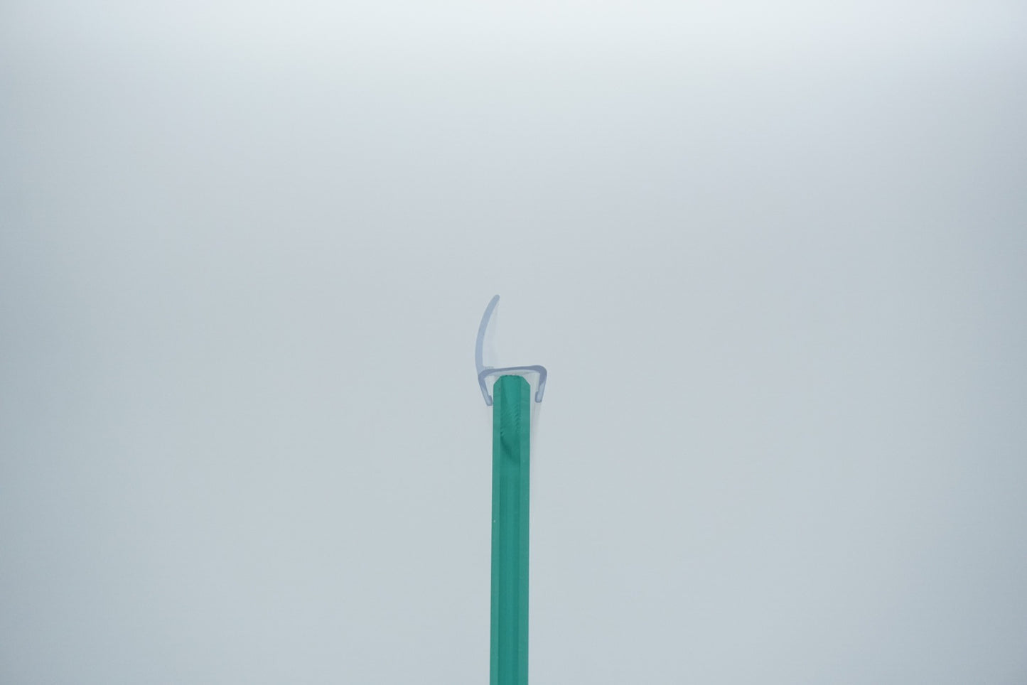 Detailaufnahme einer Anlagendichtung der Marke HÜPPE, transparentes, schmales, längliches, U-förmiges, Kunststoffprofil, mit einem Ablaufschutz an der Profilvorderseite, montiert an Glasdusche, vor weißem Hintergrund, Querschnitt.