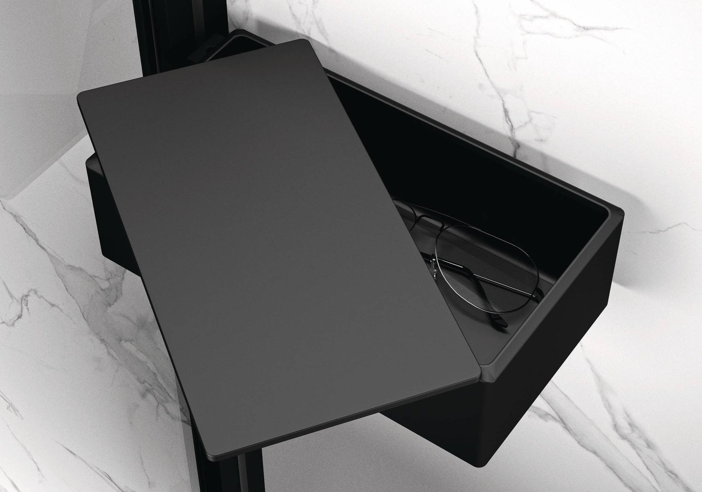 Schwarze matte Select+ Drybox der Marke HÜPPE befestigt an einer Wandleiste einer Glasdusche, mit schwarzem, offenstehendem Deckel, darin liegt eine Brille, vor einer hellen, strukturierten Wand.
