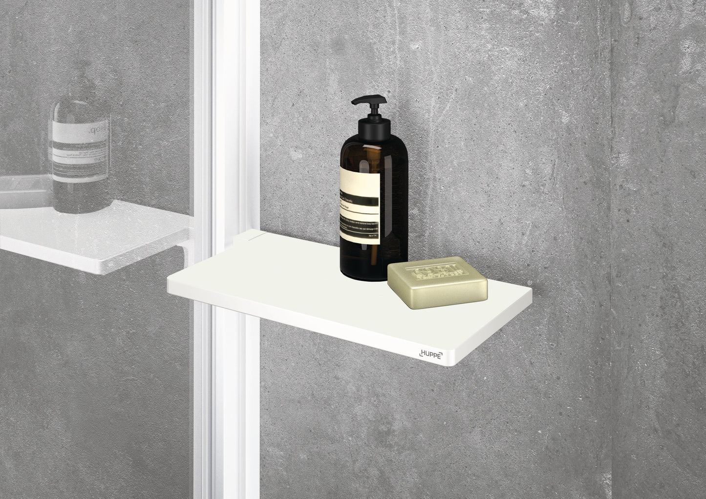 Select+ Wiper, Weiße, matte Ablage der Marke HÜPPE befestigt an einer Wandleiste einer Glasdusche, darauf steht ein Seifenspender und eine Handseife, vor einer hellgrauen strukturierten Wand.