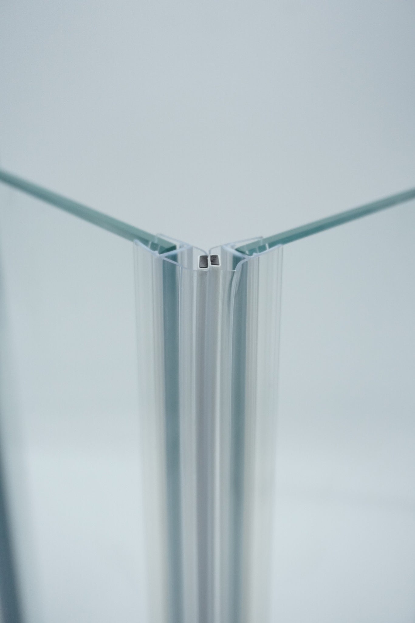Nahaufnahme, von zwei Magnetleisten der Marke HÜPPE, montiert an Glasdusche, transparente, schmale, längliche, U-förmige Kunststoffprofile, mit Magnetprofilen, an der Vorderseite, 45 Grad angewinkelt, Magneten bilden zusammen geschlossenen 90 Grad Winkel, vor weißem Hintergrund, Frontansicht Oberkante.