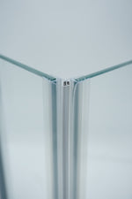 Nahaufnahme, von zwei Magnetleisten der Marke HÜPPE, montiert an Glasdusche, transparente, schmale, längliche, U-förmige Kunststoffprofile, mit Magnetprofilen, an der Vorderseite, 45 Grad angewinkelt, Magneten bilden zusammen geschlossenen 90 Grad Winkel, vor weißem Hintergrund, Frontansicht Oberkante.