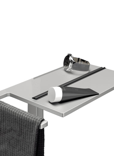 Select+ Showerboard, Klemmbares Ablagebrett der Marke HÜPPE in Silber, auf der eine Uhr, ein Duschgel und ein graues Handtuch abgelegt sind.