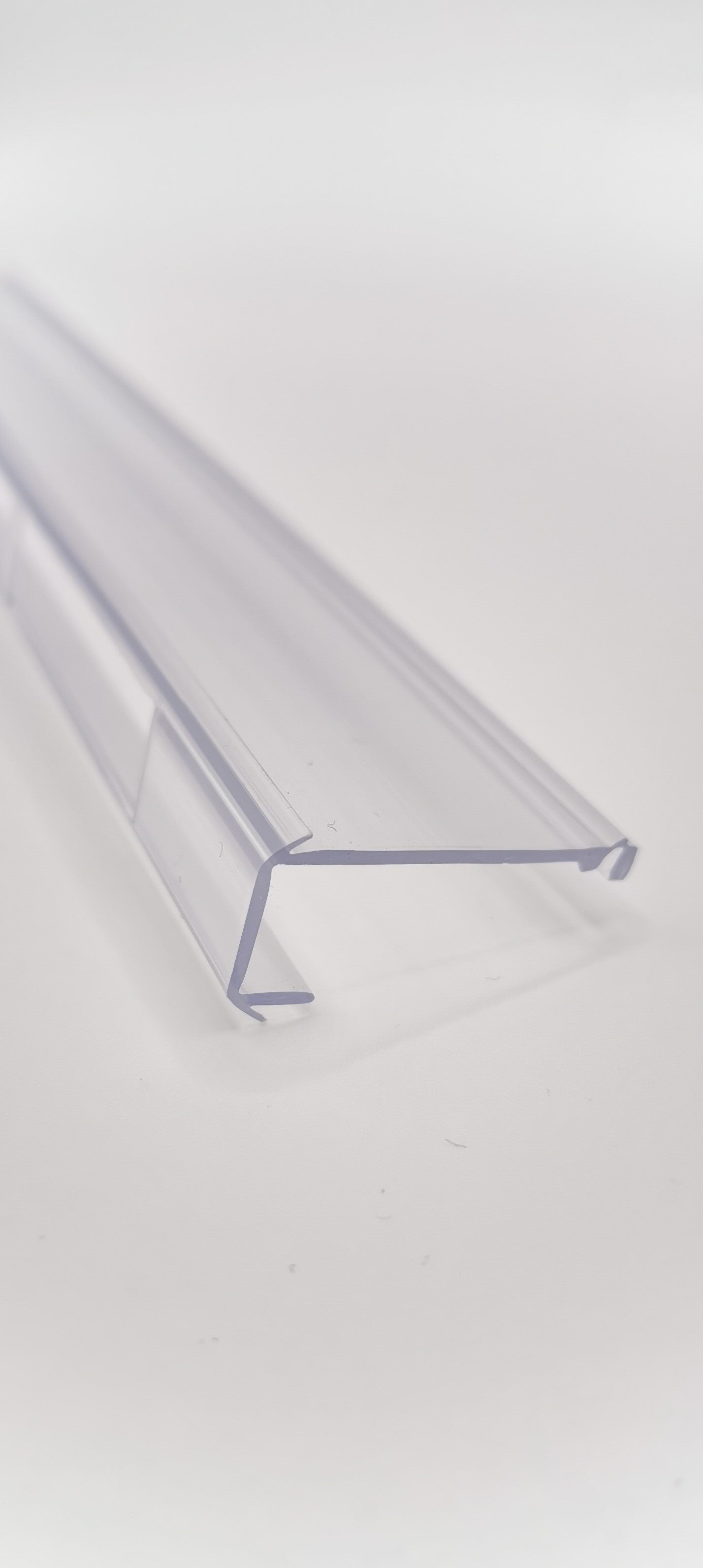 Detailaufnahme einer Glasklemmleiste der Marke HÜPPE, transparentes, schmales, längliches, Kunststoffprofil, mit einem L-förmigen Querschnitt, vor weißem Hintergrund, Seitenansicht.