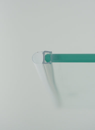 Nahaufnahme eines O-Profils der Marke HÜPPE, montiert an Glasdusche, transparentes, schmales, längliches, U-förmiges Kunststoffprofil, mit einem O-förmigen Profil an der Profilvorderseite, vor weißem Hintergrund.
