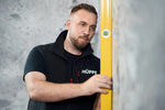 Servicetechniker der Firma HÜPPE misst mit gelber Wasserwage Toleranzen im Duschbereich auf, vor einem grauen strukturierten Hintergrund.
