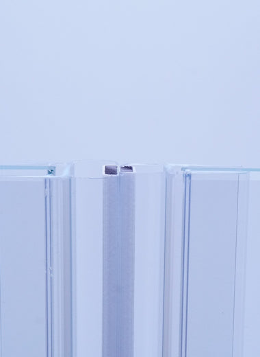 Nahaufnahme von zwei Magnetleisten der Marke HÜPPE, montiert an Glasdusche, transparente, schmale, längliche, U-förmige Kunststoffprofile, mit Magnetprofilen an der Vorderseite, Magneten bilden zusammen geschlossenen 180 Grad Winkel, vor weißem Hintergrund, Frontansicht.
