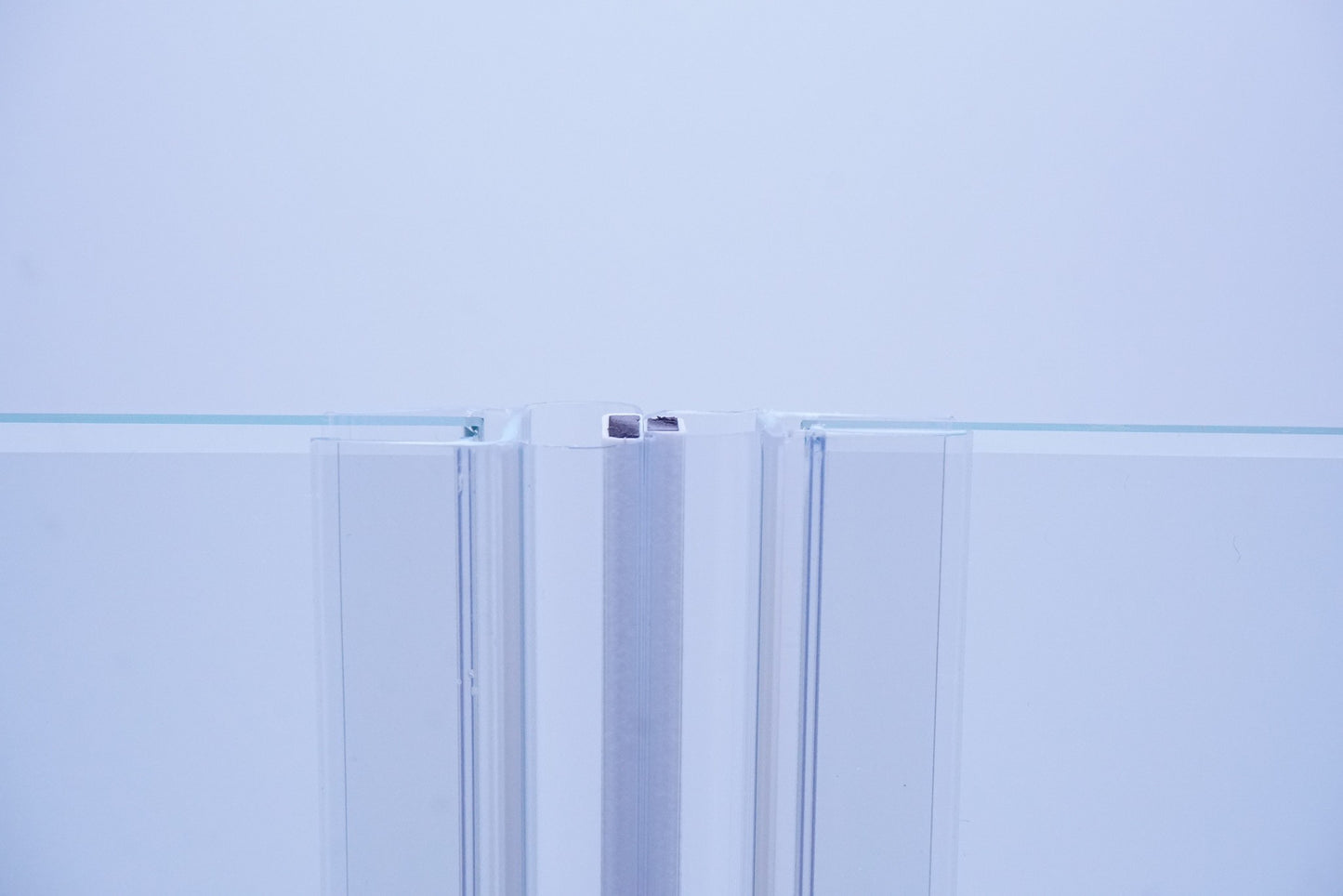 Nahaufnahme von zwei Magnetleisten der Marke HÜPPE, montiert an Glasdusche, transparente, schmale, längliche, U-förmige Kunststoffprofile, mit Magnetprofilen an der Vorderseite, Magneten bilden zusammen geschlossenen 180 Grad Winkel, vor weißem Hintergrund, Frontansicht.

