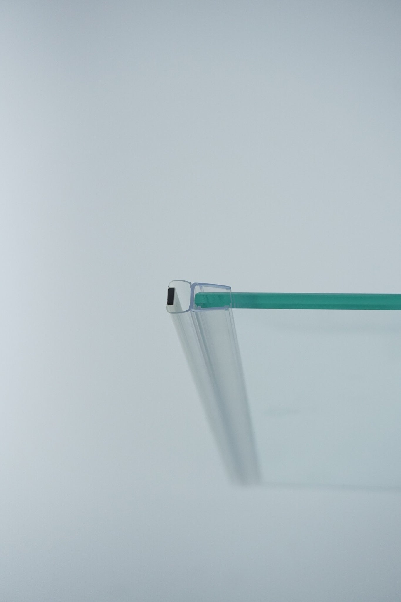 Nahaufnahme einer Magnetleiste der Marke HÜPPE, transparentes, schmales, längliches, U-förmiges Kunststoffprofil, mit einer Magnetleiste an der Profilvorderseite, montiert an Glasdusche, vor weißem Hintergrund, Seitenansicht rechts.